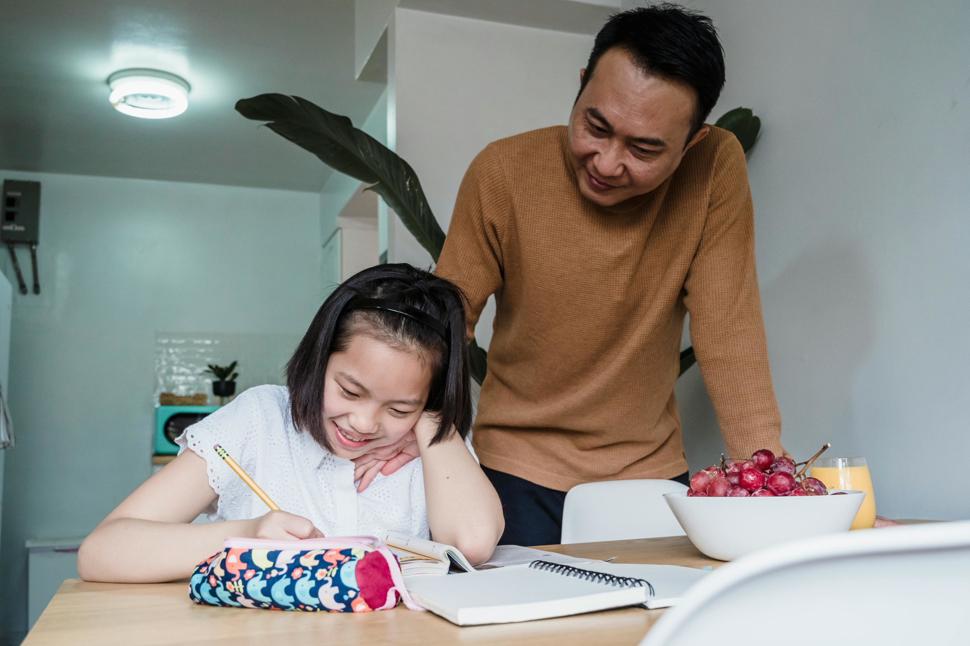 a father looking at his daughter doing homework